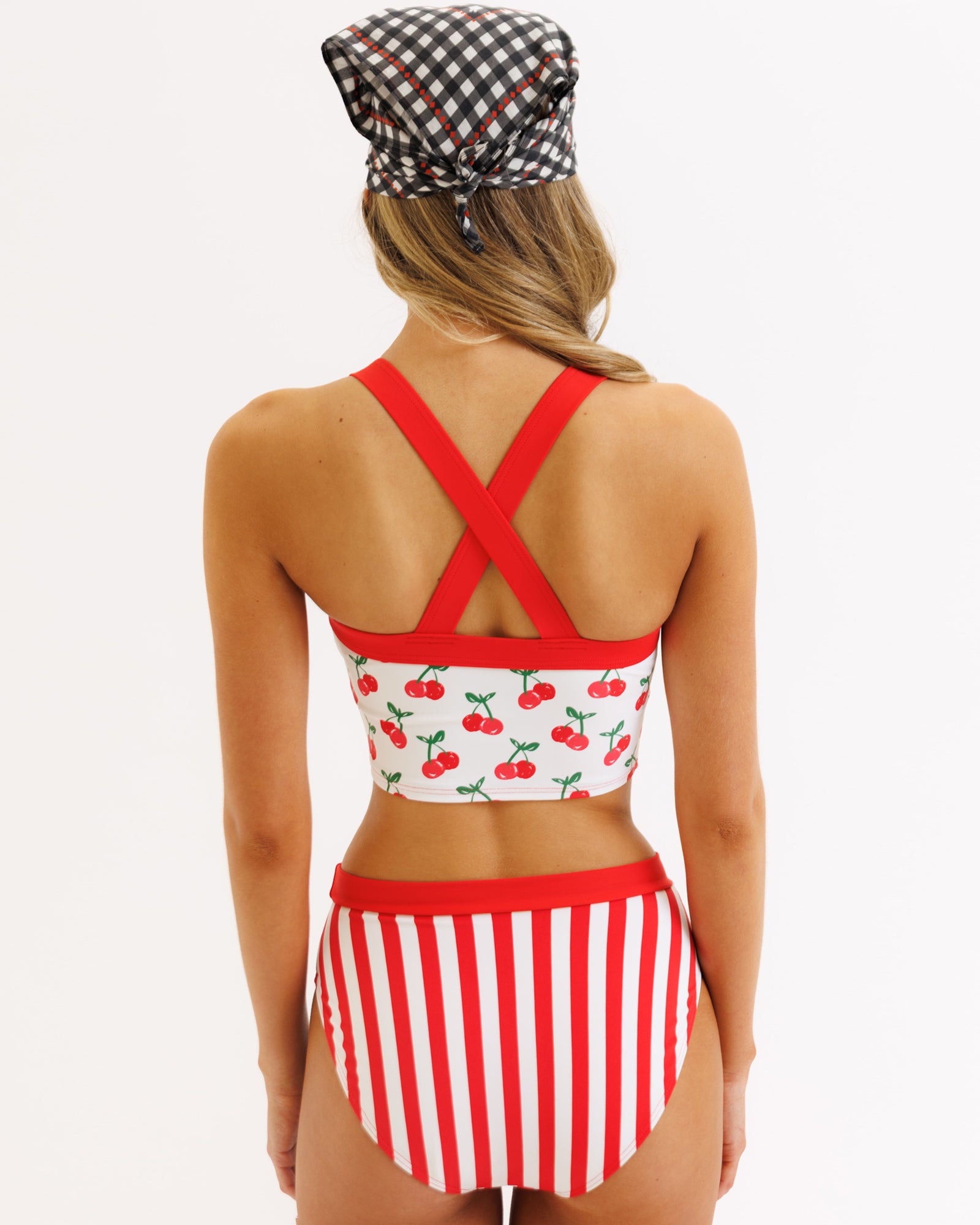 Woman wearing a red and white striped bikini with cherry pattern on a plain background