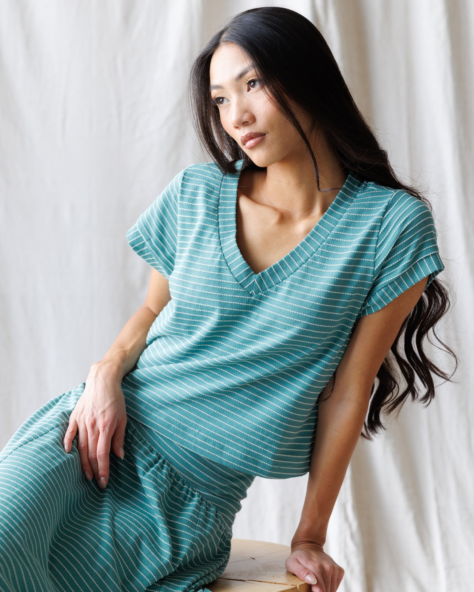 Woman wearing a teal dress sitting against a white curtain