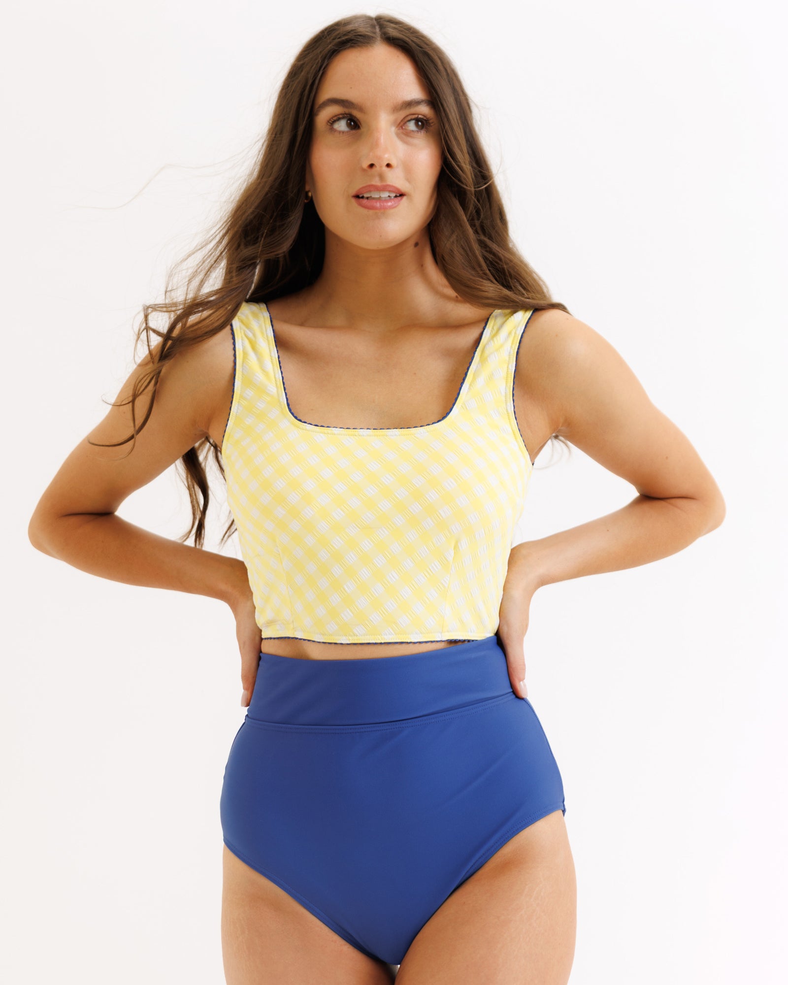 Woman wearing a yellow patterned top and blue high-waisted swimsuit on a white background