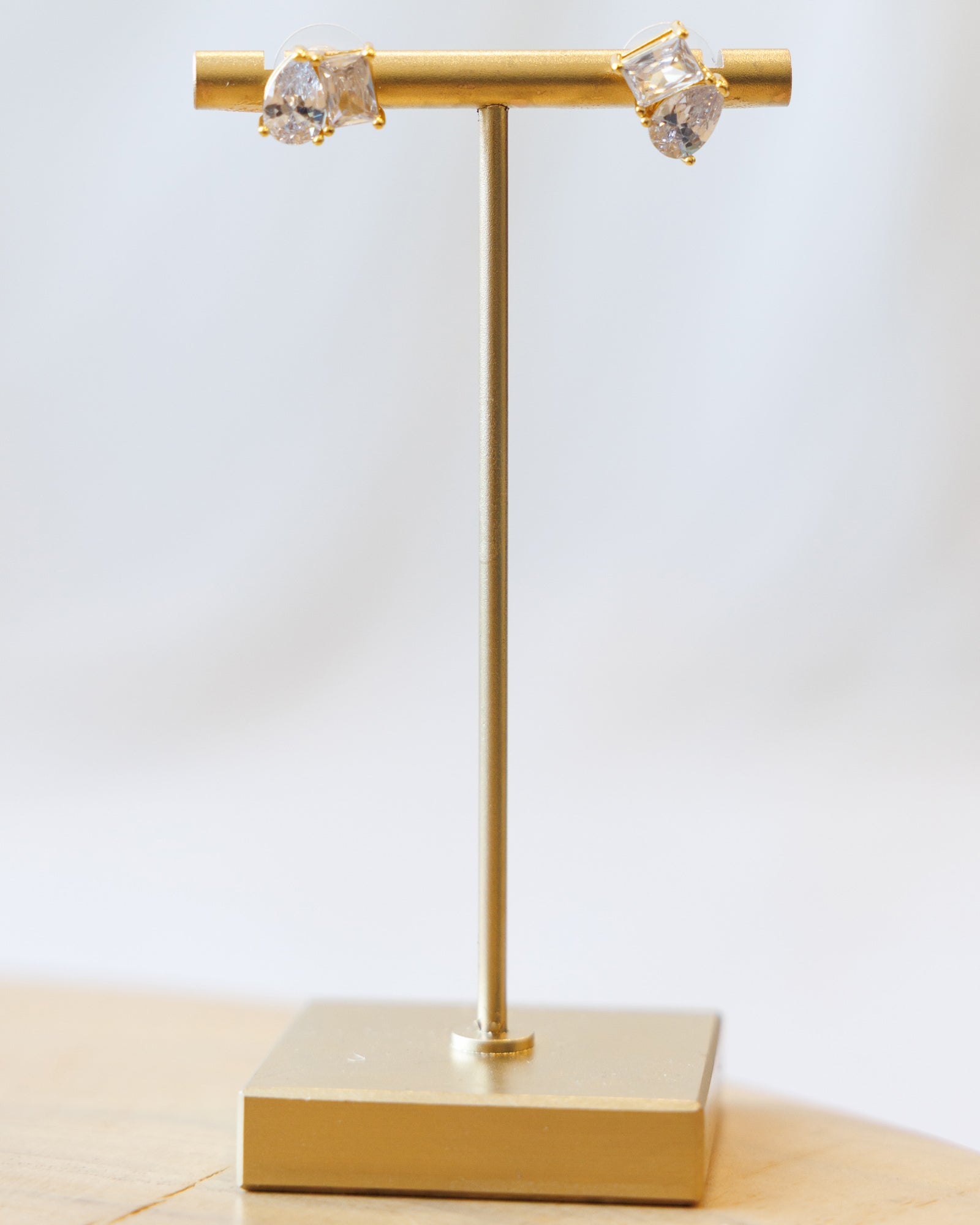 Gold earring stand with two crystal earrings on a light background