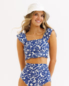 Woman wearing a blue floral bikini set and white bucket hat on a white background