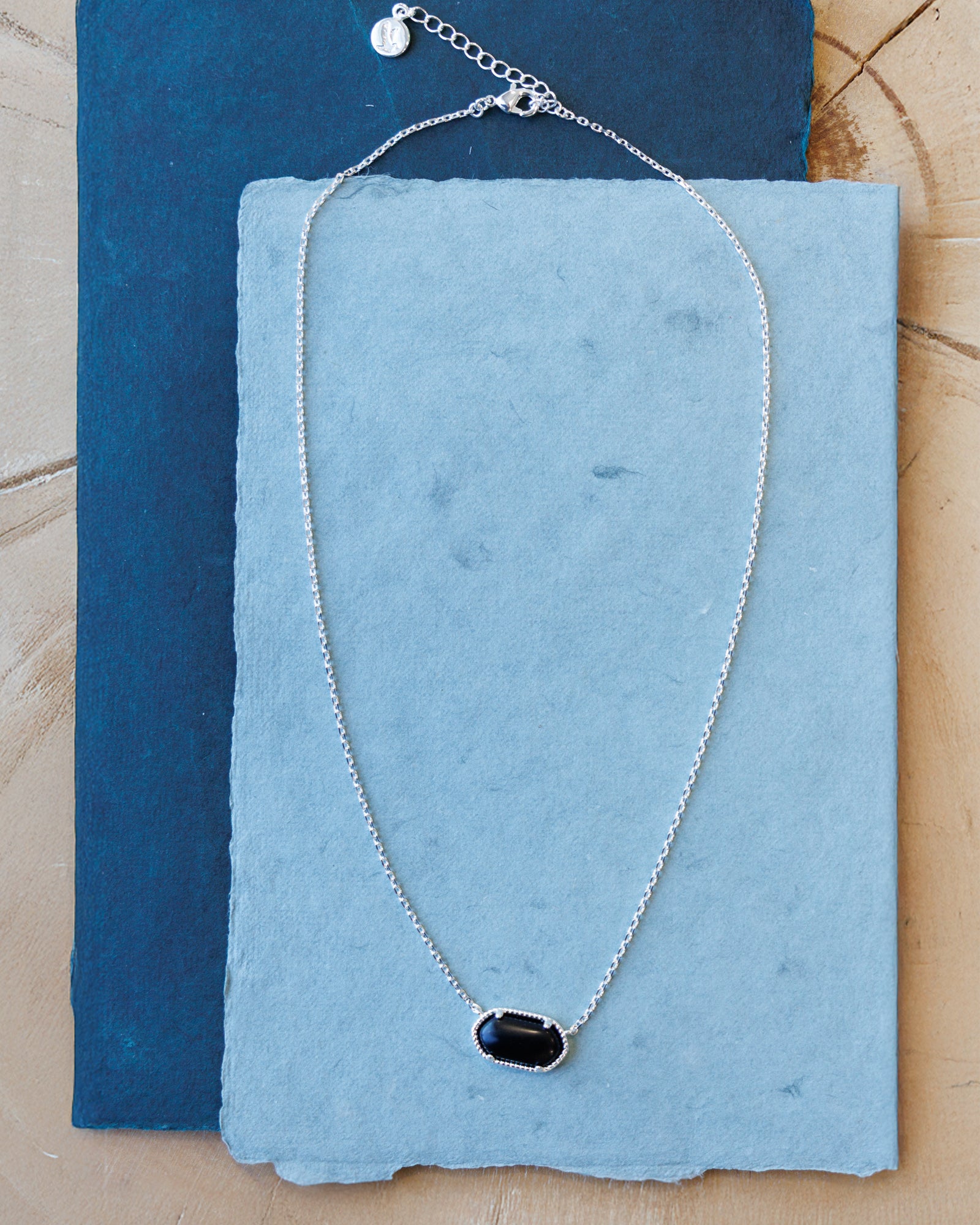 Silver necklace with a black pendant on a blue fabric background