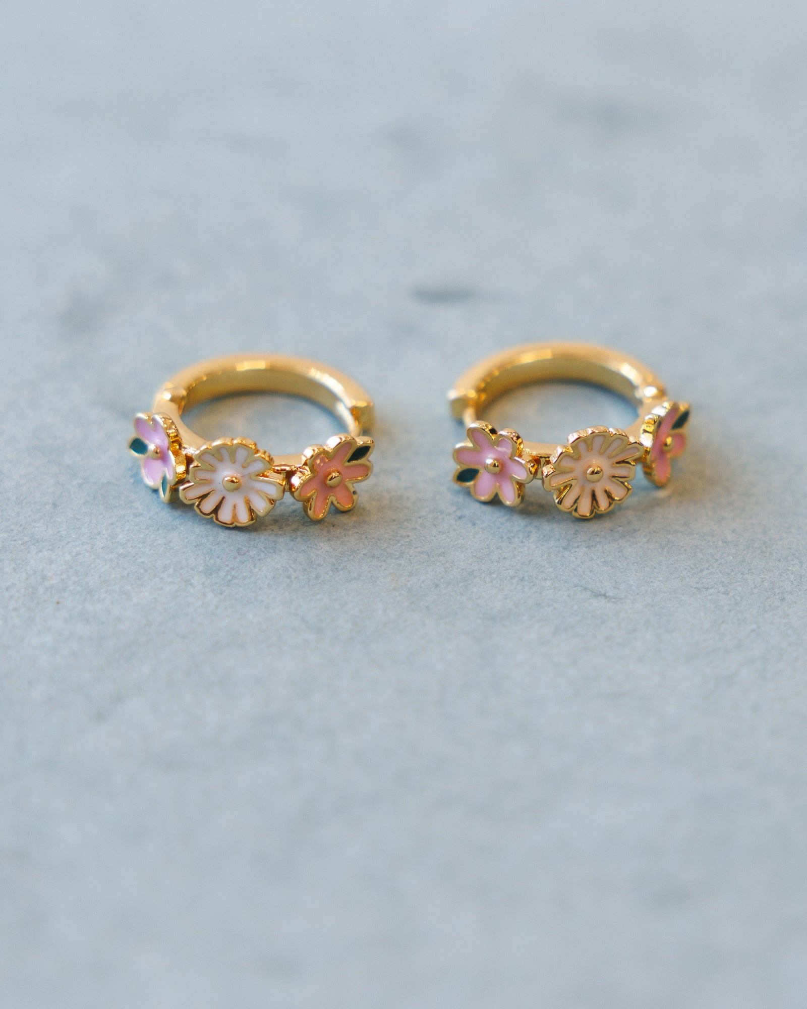 Gold hoop earrings with floral designs on a light blue background