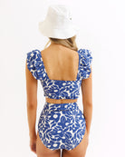 Woman wearing a blue floral two-piece swimsuit and white bucket hat on a white background