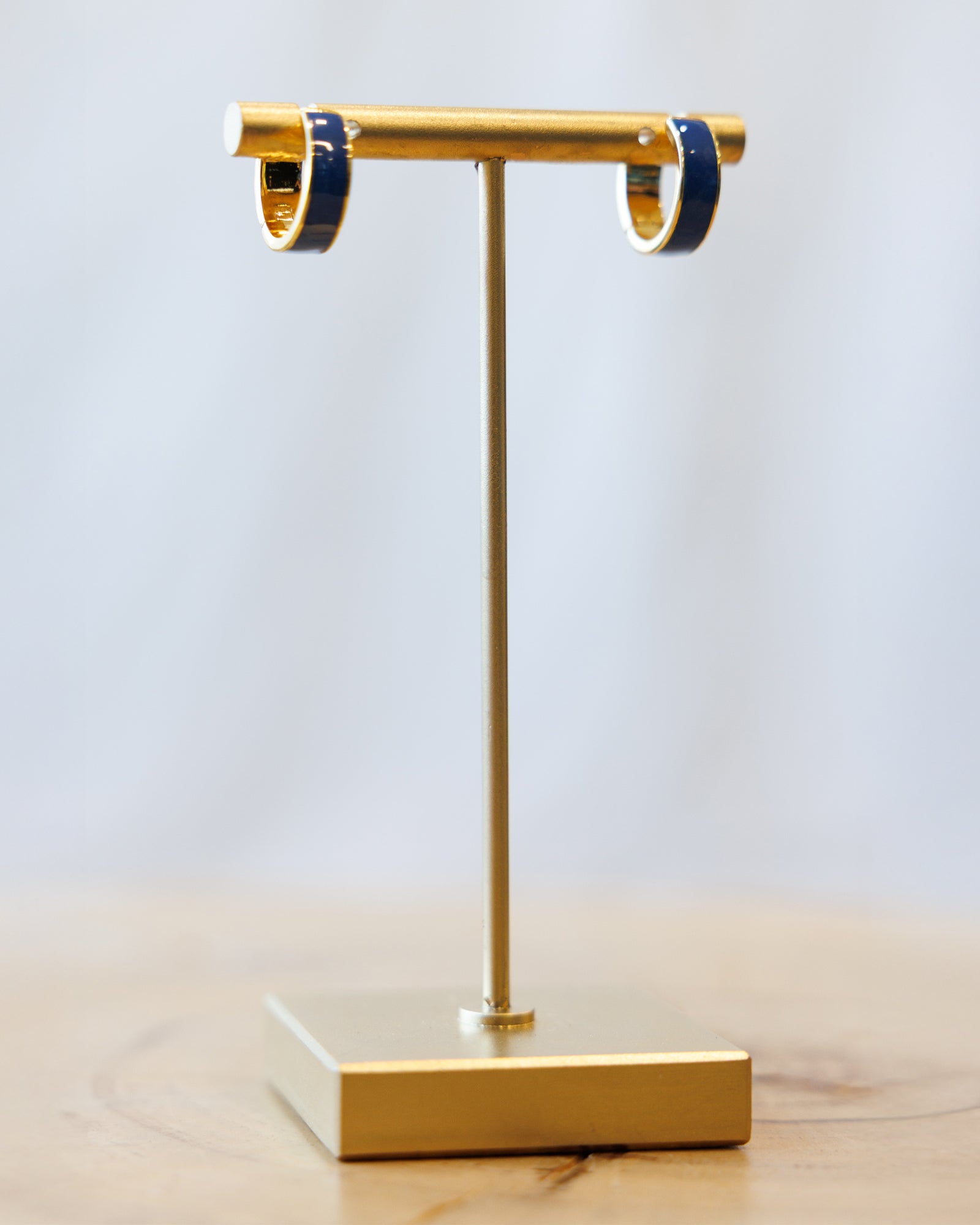 Gold earring stand with blue-rimmed earrings on a light gray background