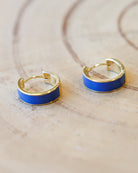 Gold hoop earrings with blue enamel accents on a light wooden surface.