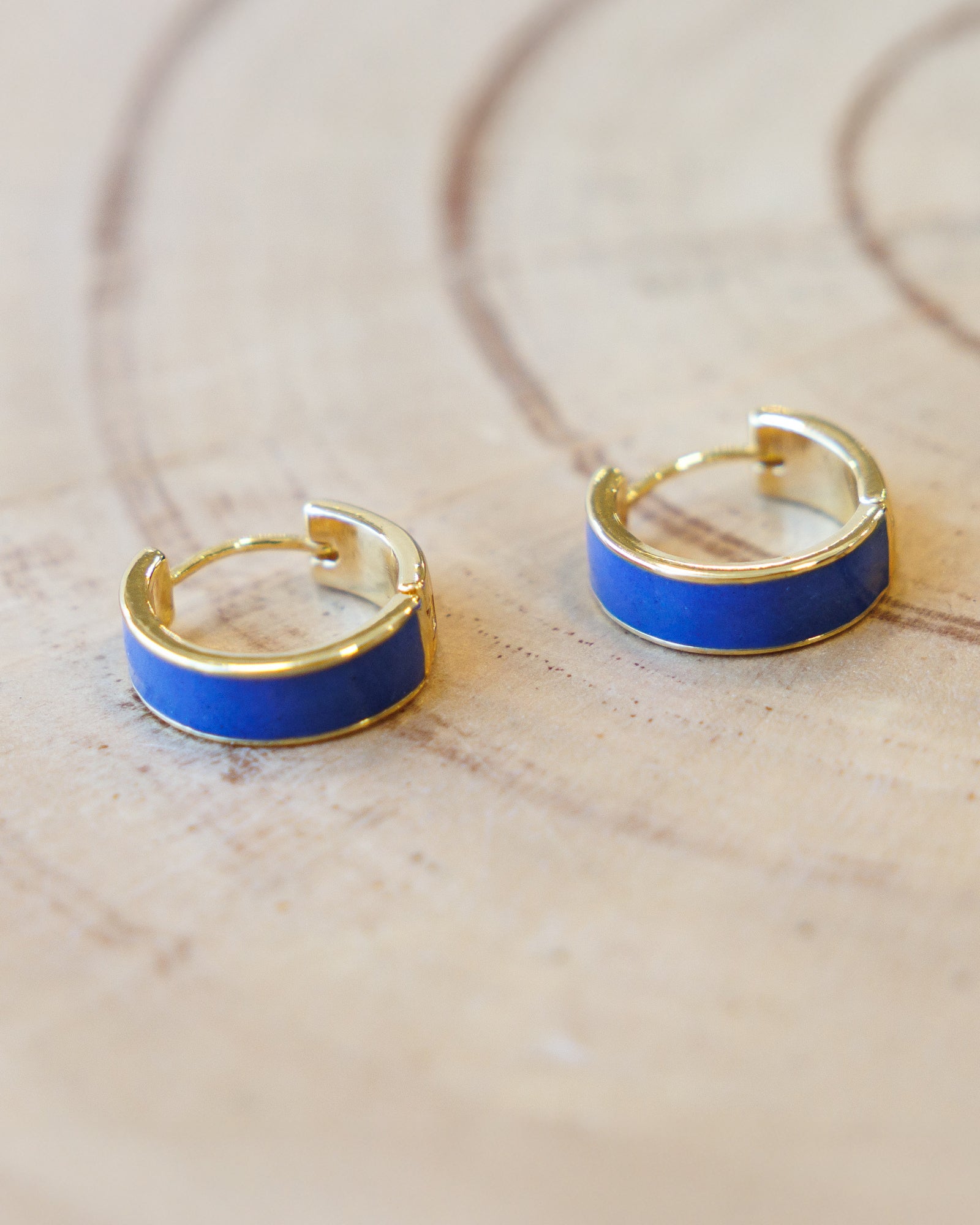 Gold hoop earrings with blue enamel accents on a light wooden surface.