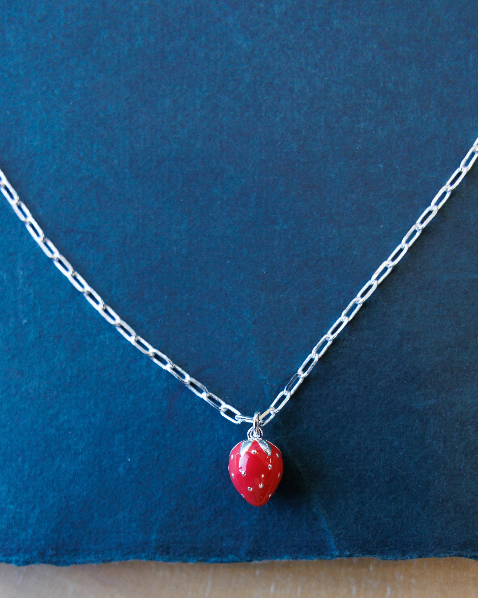 Necklace with a red strawberry-shaped pendant on a blue background