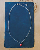 Silver necklace with a red pendant on a blue fabric background