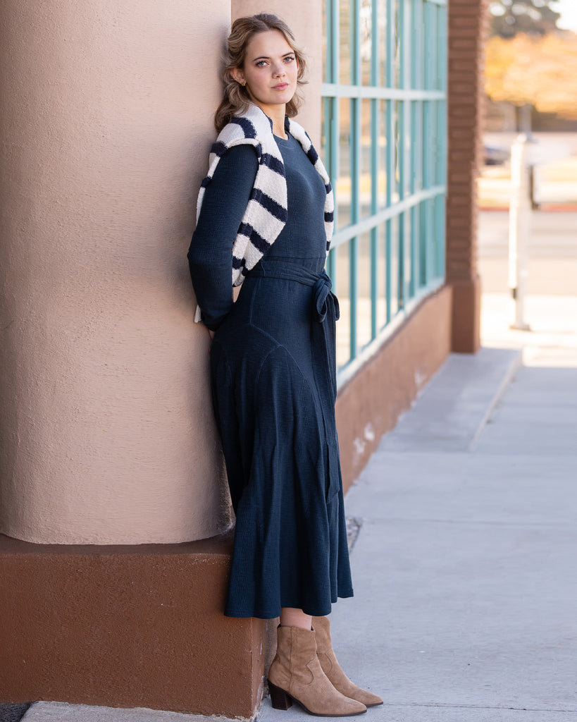 Model wearing a blue knit long sleeve fit and flare style dress that is midi length.