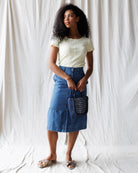 Woman wearing a white t-shirt and blue denim skirt with a patterned bag against a white background