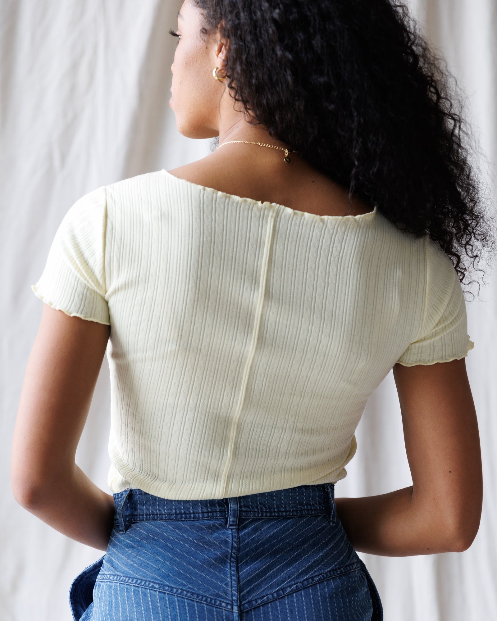 Person wearing a light green ribbed top and blue pants against a neutral background