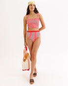 Woman wearing a red and white striped bikini holding a bag on a white background