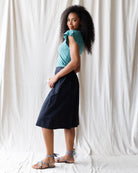 Woman wearing a blue top and black skirt against a white curtain background