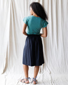 Person wearing a teal top and black skirt against a white curtain background