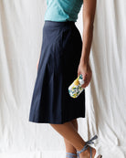 Person wearing a navy skirt and holding a colorful bottle against a white curtain background