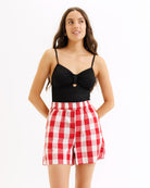 Woman wearing a black top and red checkered shorts on a white background