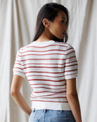 Woman wearing a white and red striped crochet top against a neutral background