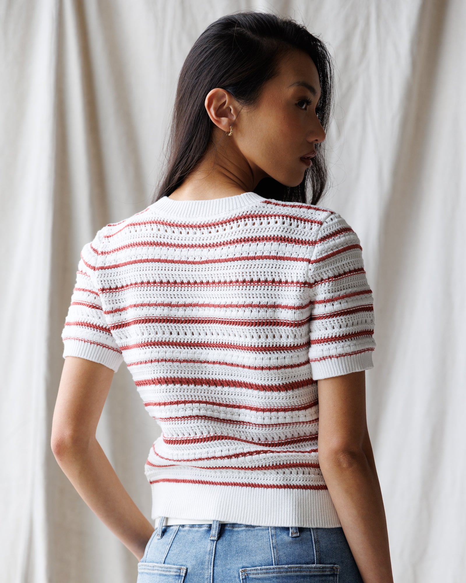 Woman wearing a white and red striped crochet top against a neutral background