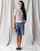 Woman wearing a striped shirt and denim shorts against a white curtain background