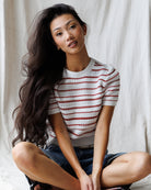 Woman wearing a striped shirt sitting on the floor against a plain background