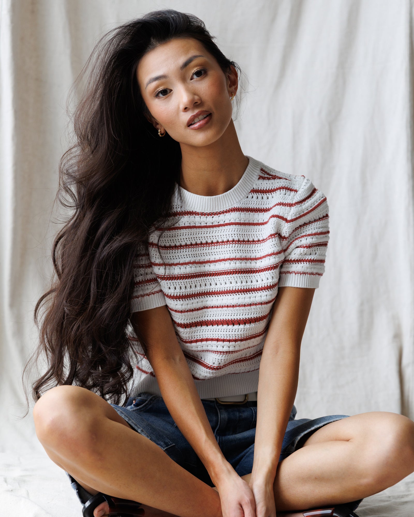 Woman wearing a striped shirt sitting on the floor against a plain background