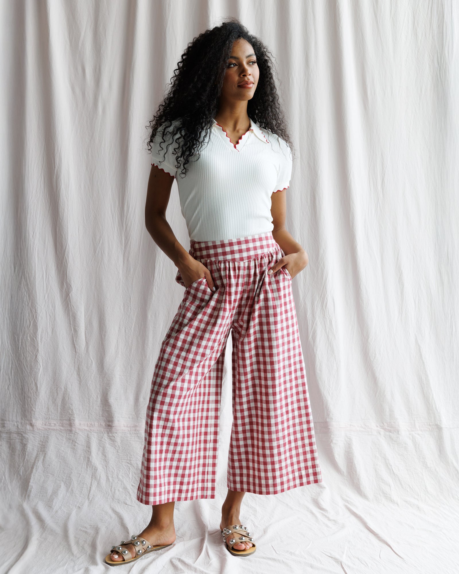 Woman wearing a white top and red checkered pants against a plain background