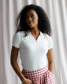 Woman wearing a white top with red trim and red checkered pants against a neutral background