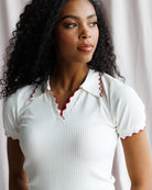 Woman wearing a white ribbed top with red trim against a neutral background