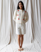 Woman wearing a white cardigan with red cherry patterns on a plain background