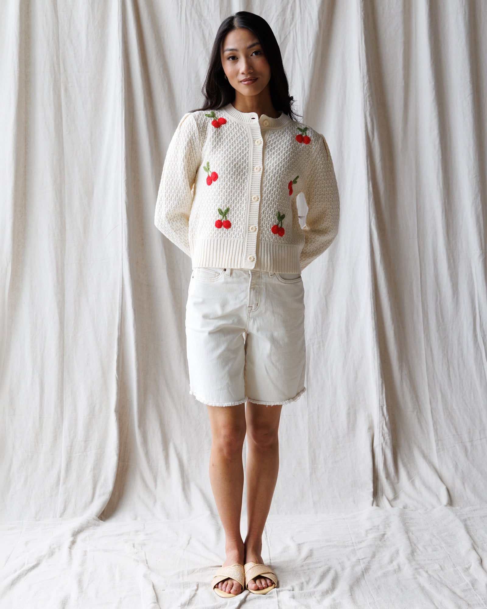 Woman wearing a white cardigan with red cherry patterns on a plain background