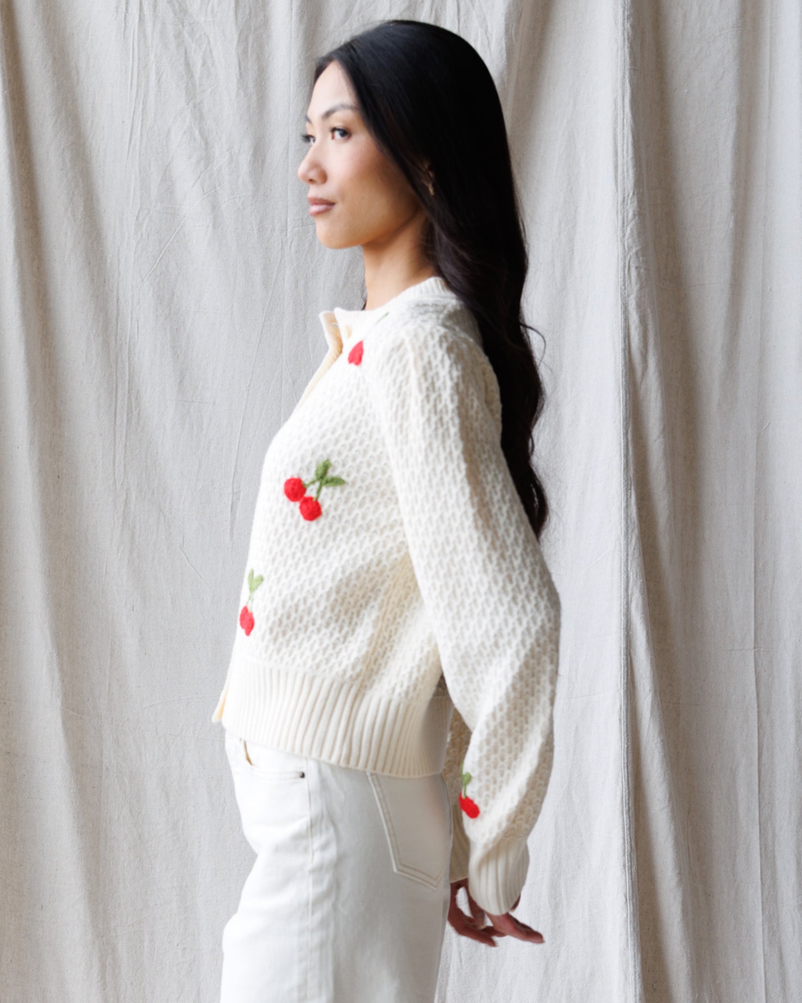 Woman wearing a white sweater with red cherry patterns against a plain background