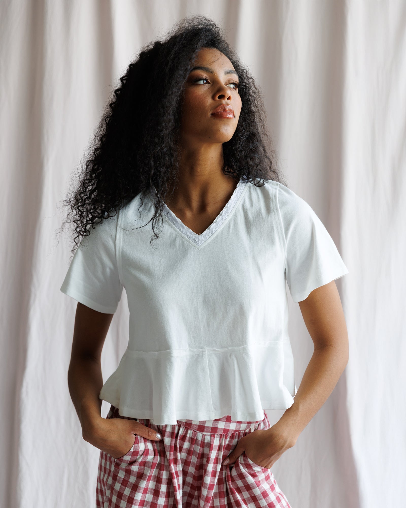 Woman wearing a white blouse and red checkered pants against a plain background