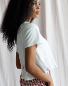 Woman wearing a white t-shirt and red checkered shorts standing against a white curtain.