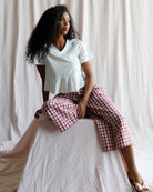 Woman wearing a white top and red checkered pants sitting on a white surface with a white curtain background.