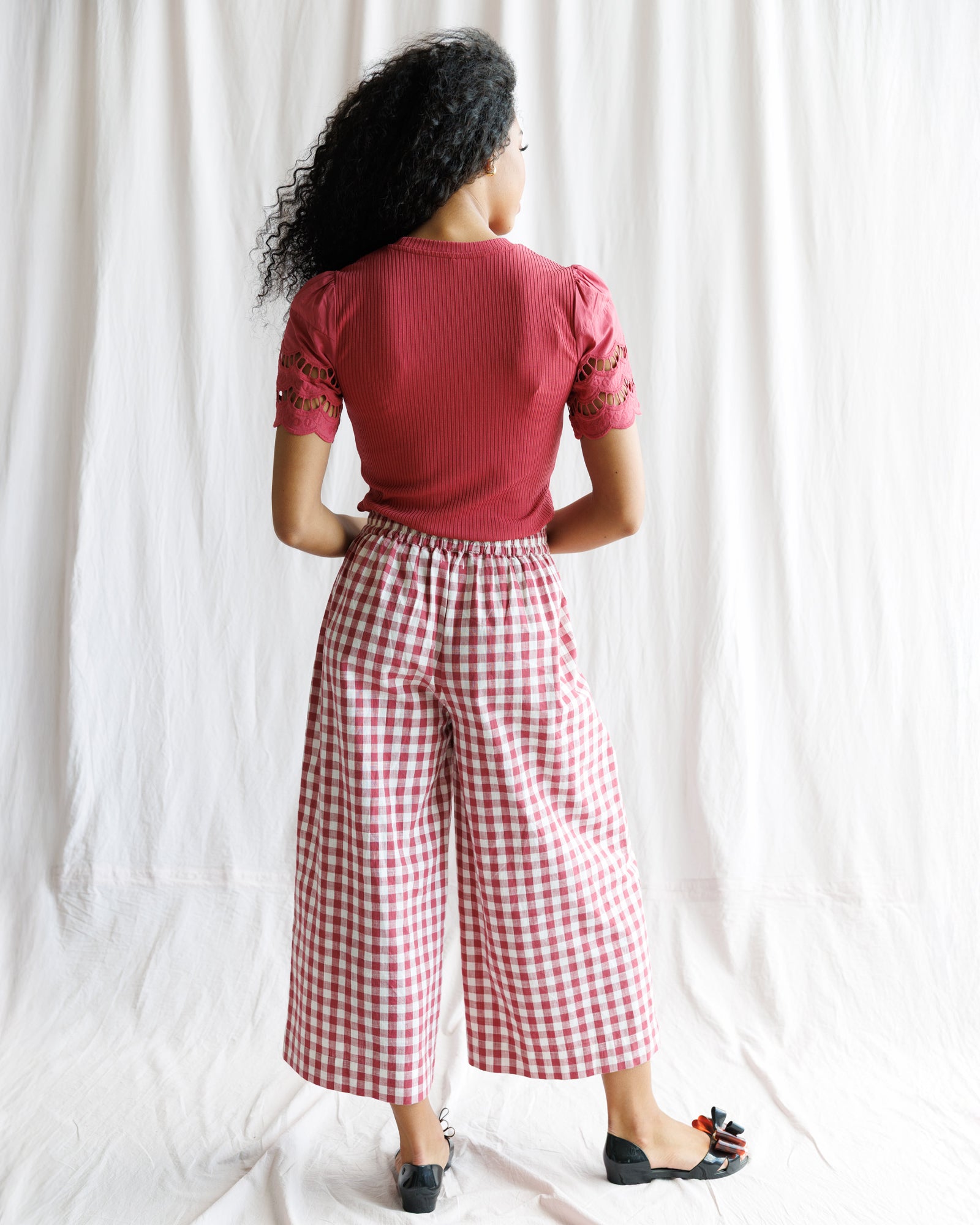Person wearing a red top and red and white checkered pants against a white background