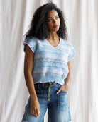 Woman wearing a light blue floral-patterned sleeveless top against a white curtain background