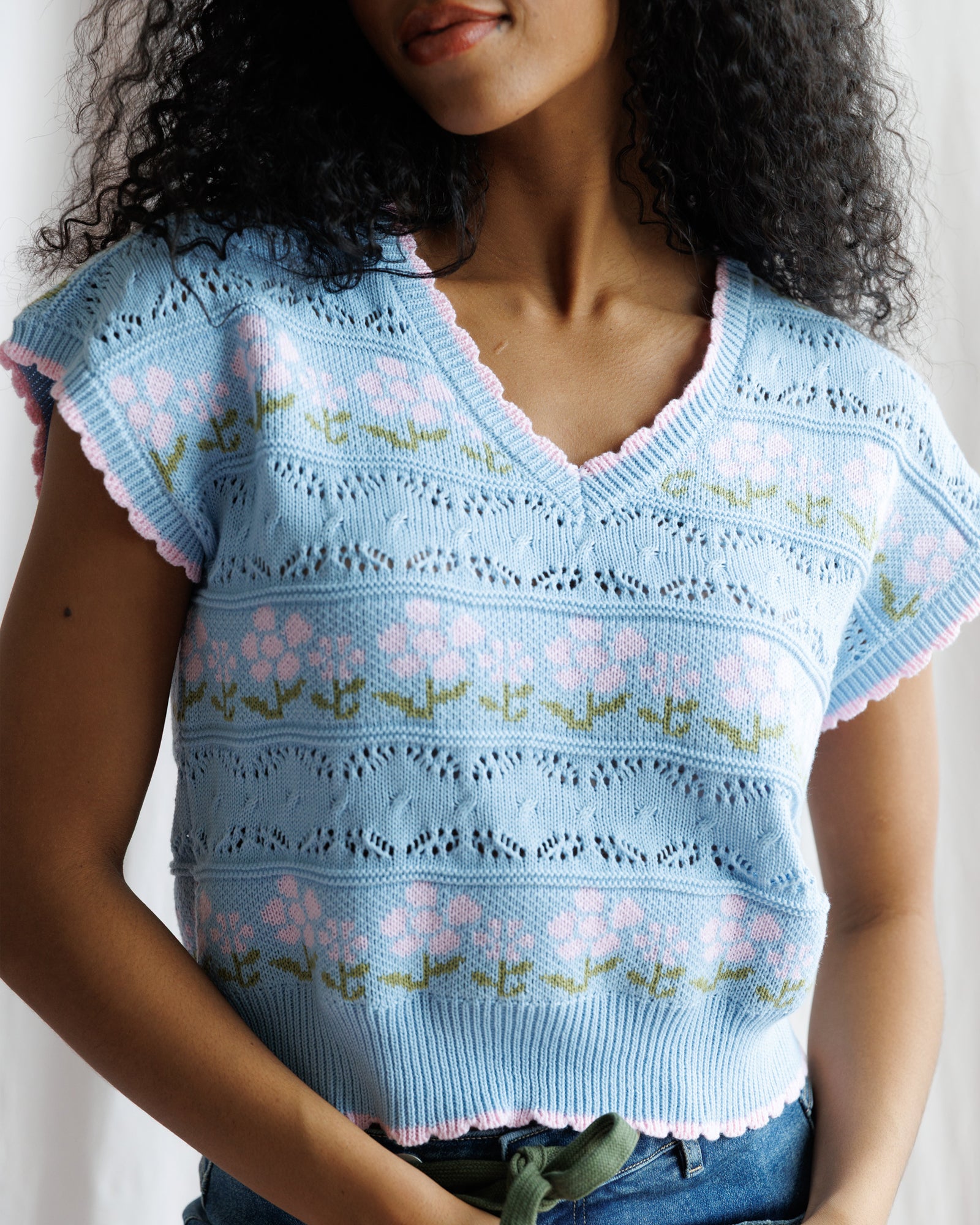 Woman wearing a light blue floral-patterned knit top against a plain background