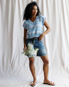 Woman wearing a light blue sleeveless top and denim shorts, holding flowers against a white background