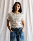 Woman wearing a patterned top and blue jeans against a plain background