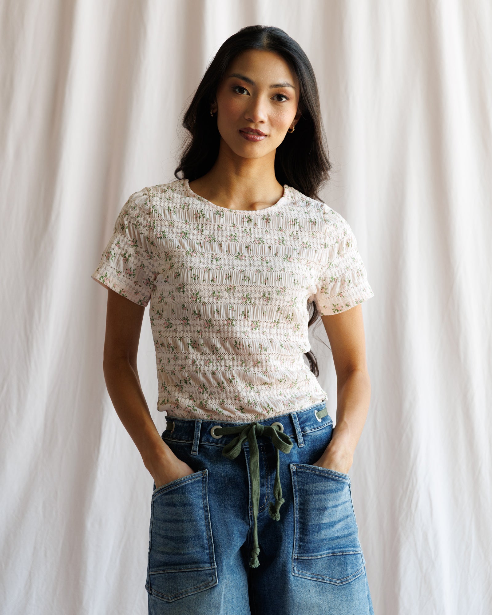 Woman wearing a patterned top and blue jeans against a plain background