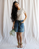Woman wearing a floral top and denim skirt holding flowers against a white background