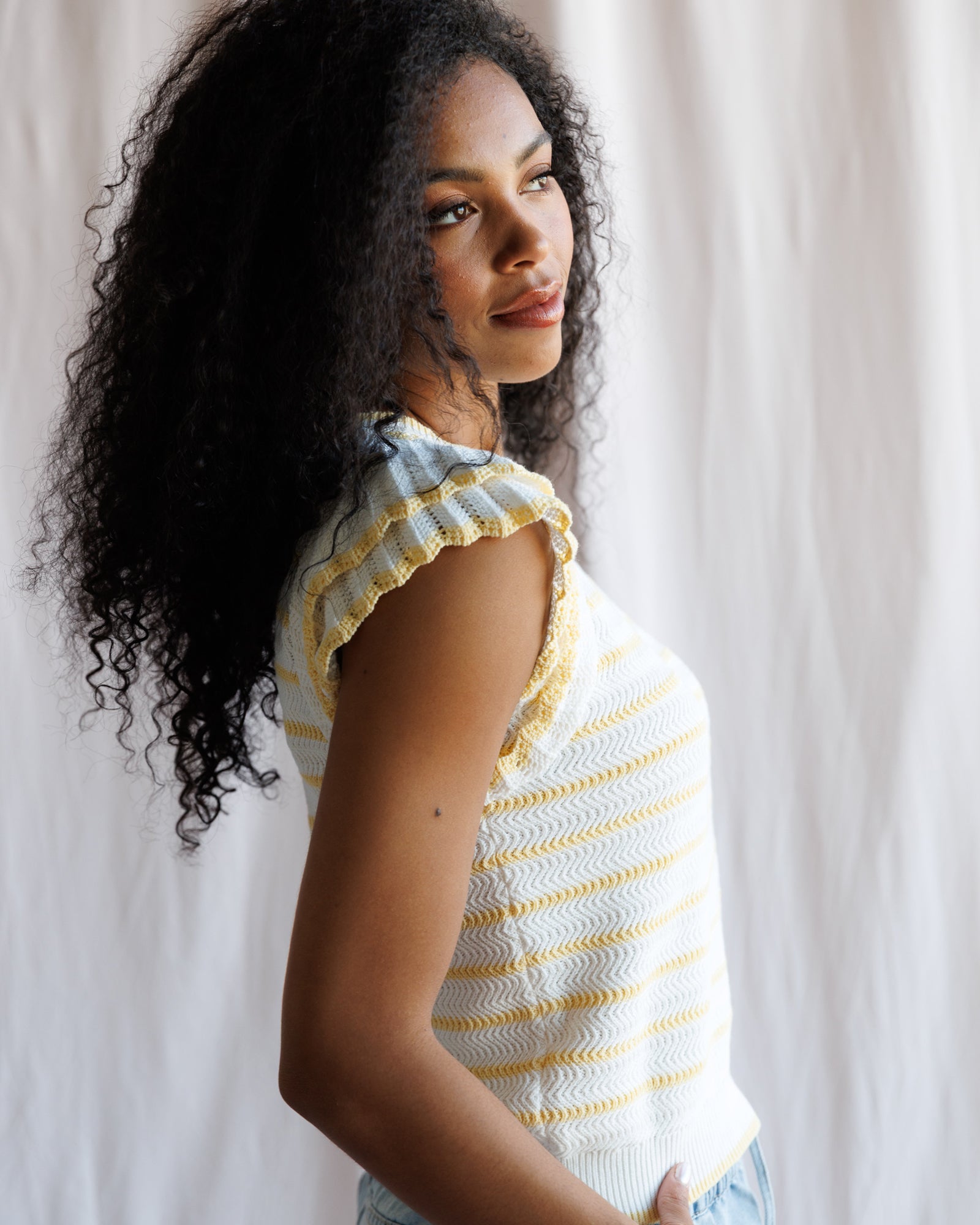 Woman wearing a white and yellow striped sleeveless top against a neutral background
