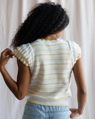 Person wearing a white and yellow striped shirt with ruffled sleeves against a neutral background