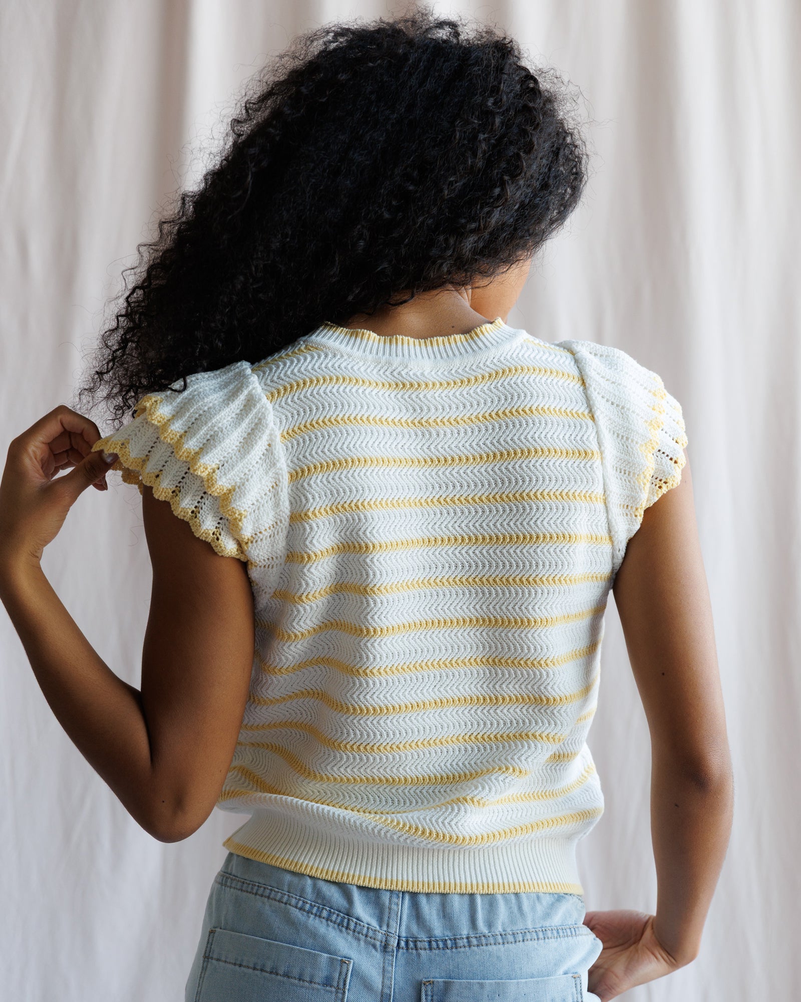 Person wearing a white and yellow striped shirt with ruffled sleeves against a neutral background