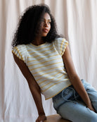 Woman wearing a yellow and white striped top sitting against a plain background