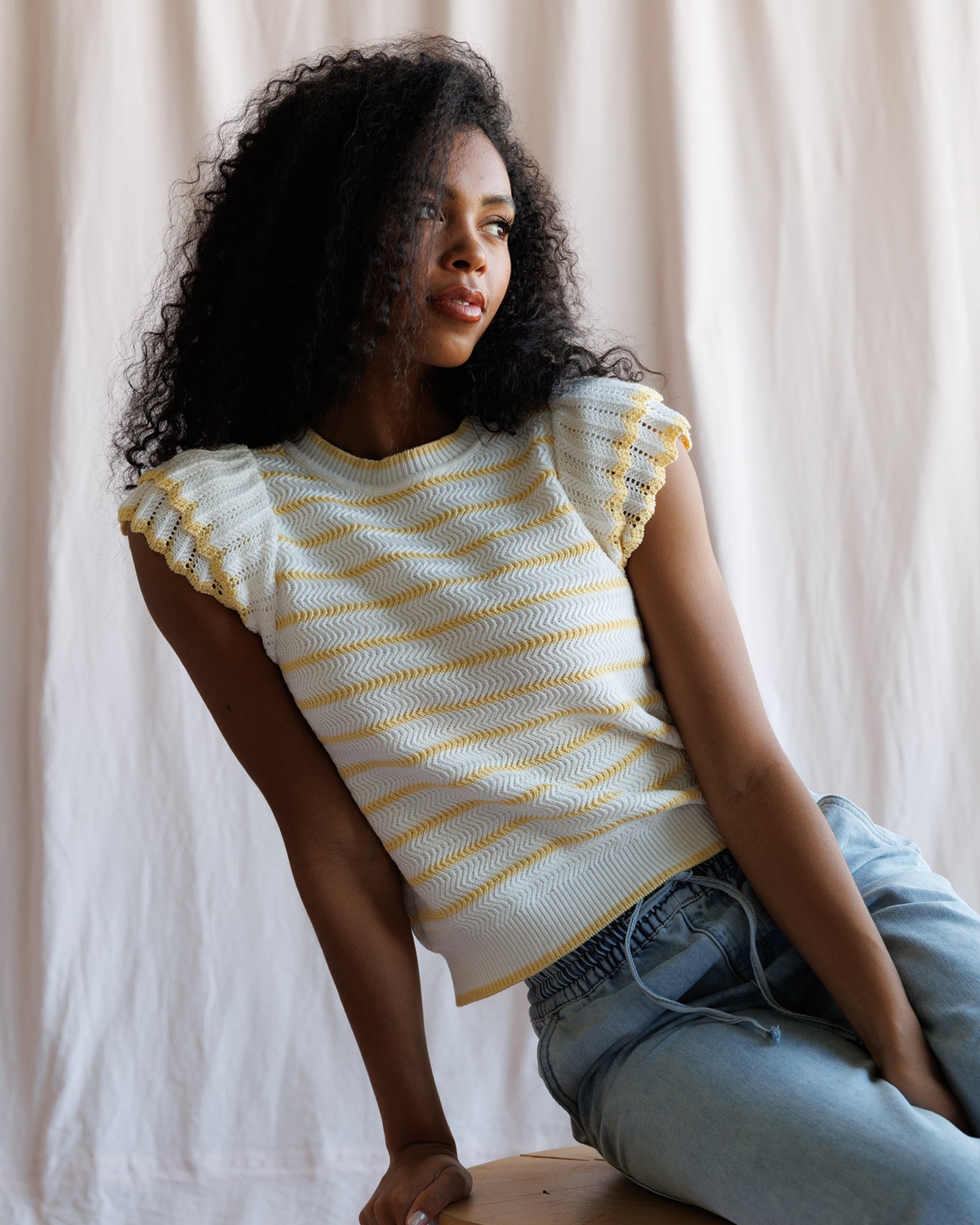 Woman wearing a yellow and white striped top sitting against a plain background