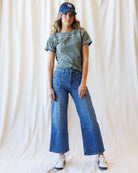 Woman wearing a green tshirt with blue jeans and a baseball cap standing in front of a canvas backdrop