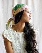 Woman wearing a colorful headscarf with a white lace top against a light background