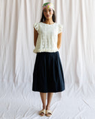 Woman wearing a white lace top and black skirt against a plain background